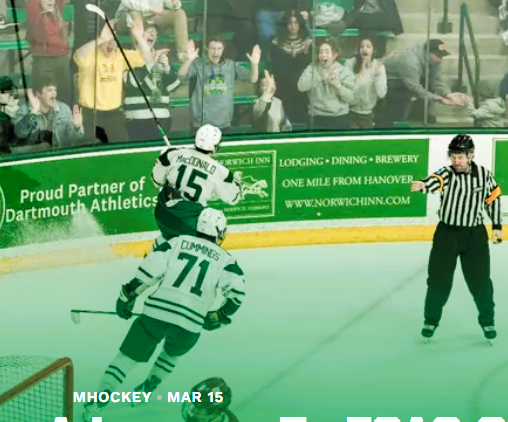 Hockey players in green uniforms celebrate on the ice as fans cheer in the stands; a referee skates nearby pointing with his arm raised.