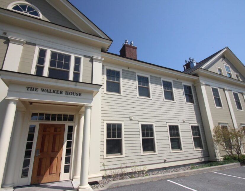 A beige, two-story building with white trim and columns, labeled The Walker House, under a clear blue sky.
